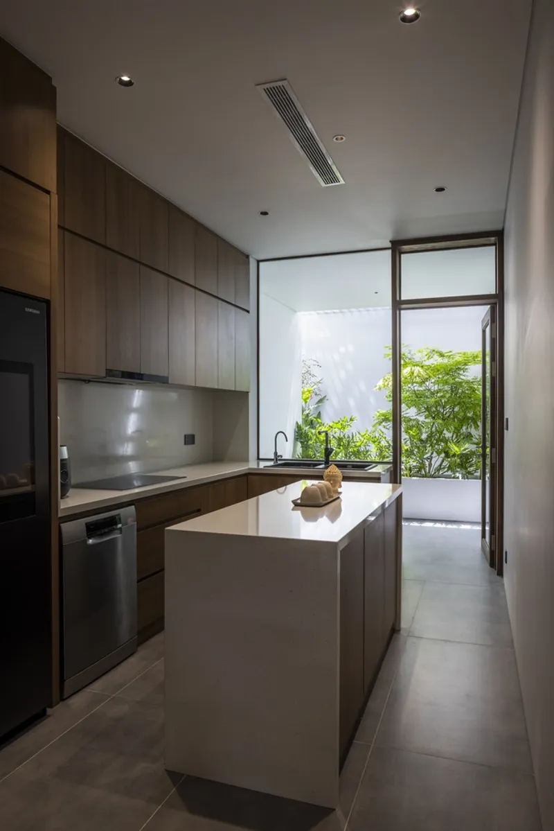 Galley kitchen with timber cabinetry and white island opening to a planted courtyard through glazed doors