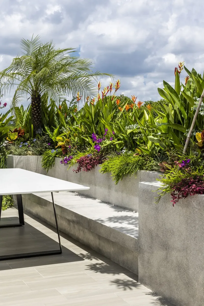 Rooftop planter with cascading tropical plants and palms beneath a cloudy sky