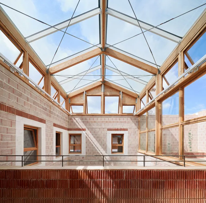 Glazed courtyard with timber frame structure and steel tension rods above terracotta and pink brick walls