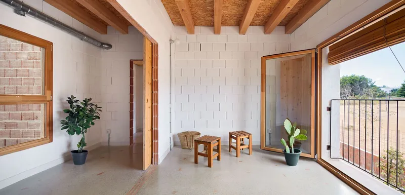 Interior room with exposed timber beams, white block walls and potted plants near an open balcony door