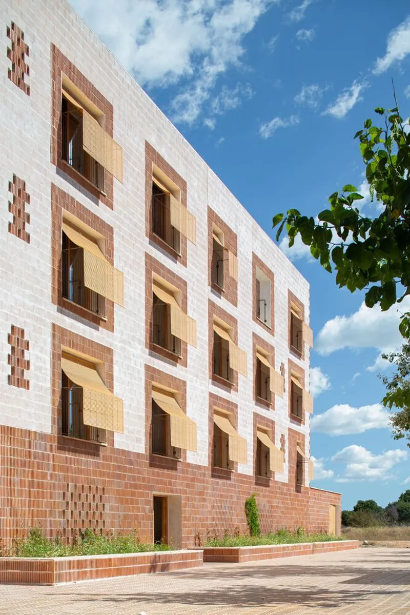 Street facade with patterned terracotta and pink brick cladding under a blue sky with scattered clouds