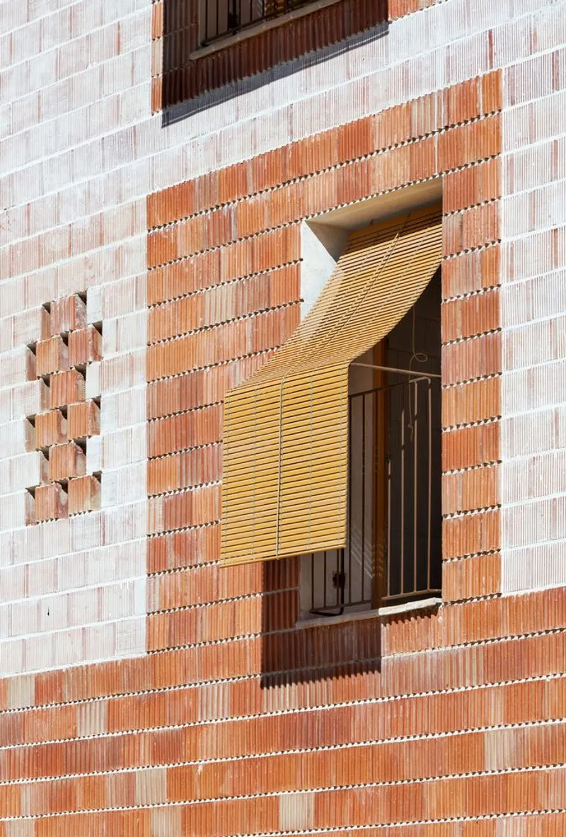 Facade detail showing timber louvered shutter within a pink and terracotta patterned brick opening