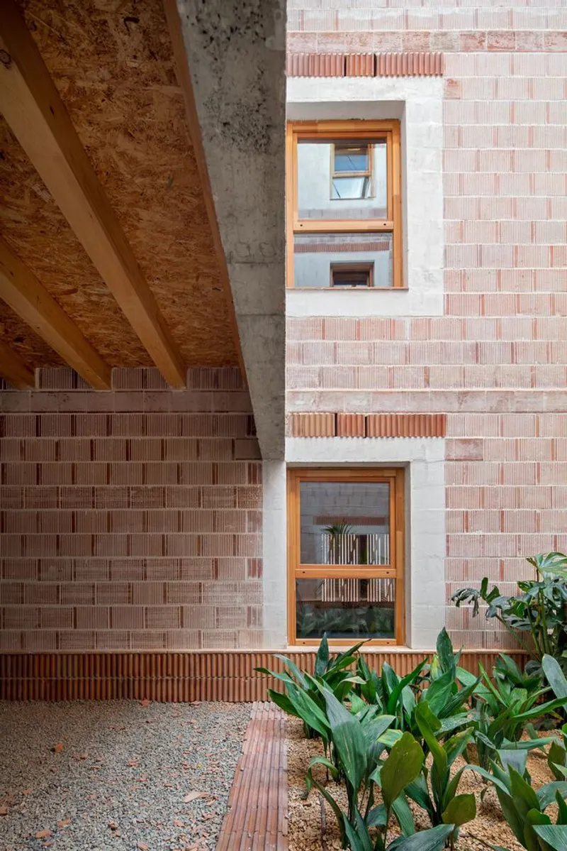 Courtyard view showing stacked timber-framed windows in a pink brick facade with concrete column and planted beds