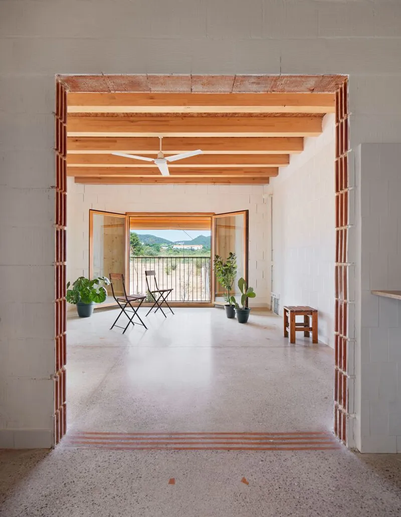 Interior view through a brick-framed doorway with exposed timber ceiling beams and balcony door overlooking distant hills