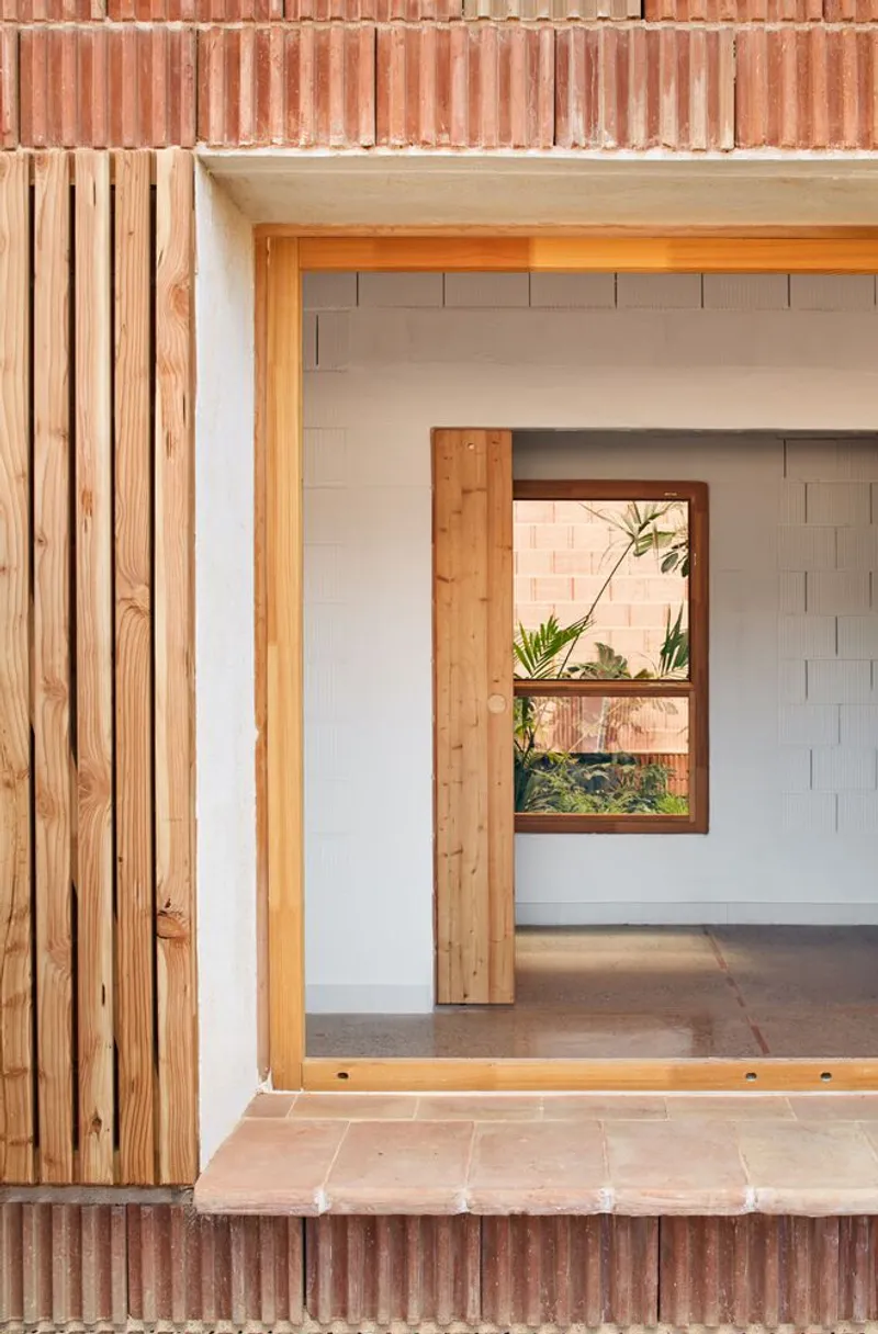 Threshold detail showing timber shutters, pink brick surround, and framed window opening with planted courtyard view