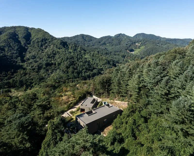 Aerial view of the dark-roofed compound nestled into a forested mountain slope under clear blue sky