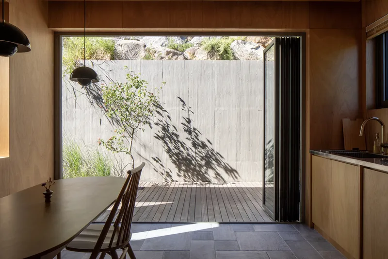 Timber-lined dining area opening to timber deck courtyard with textured concrete wall and shadows