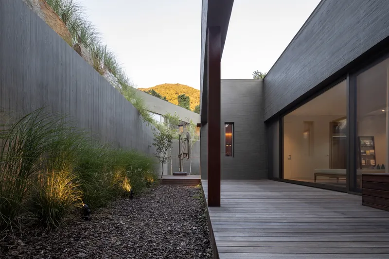 Timber deck courtyard framed by textured concrete walls with planted grasses and hillside at dusk