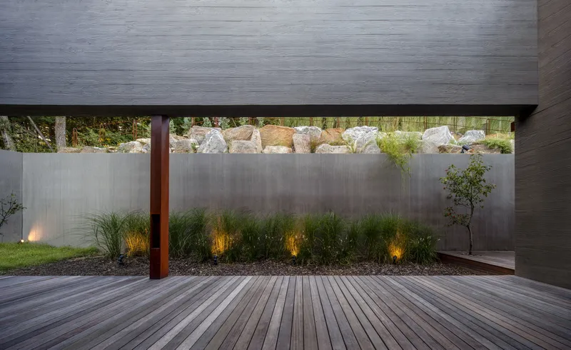 Timber deck courtyard at dusk with uplighting illuminating grasses against board-formed concrete walls