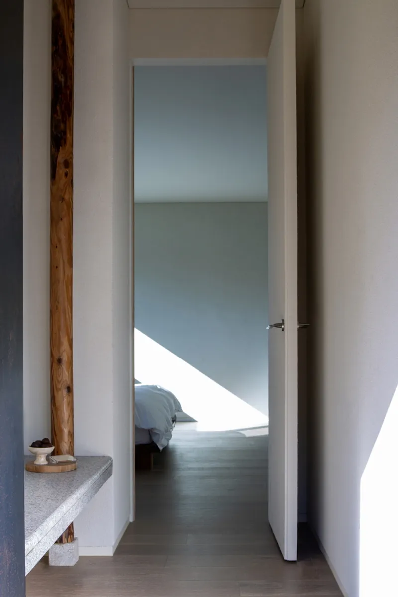 Narrow hallway with natural timber post and stone shelf leading toward bedroom with angled sunlight