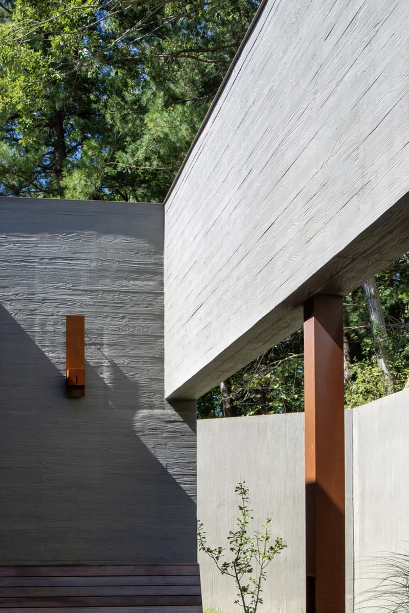 Exterior view of angled roof overhang supported by Corten steel column amid surrounding trees