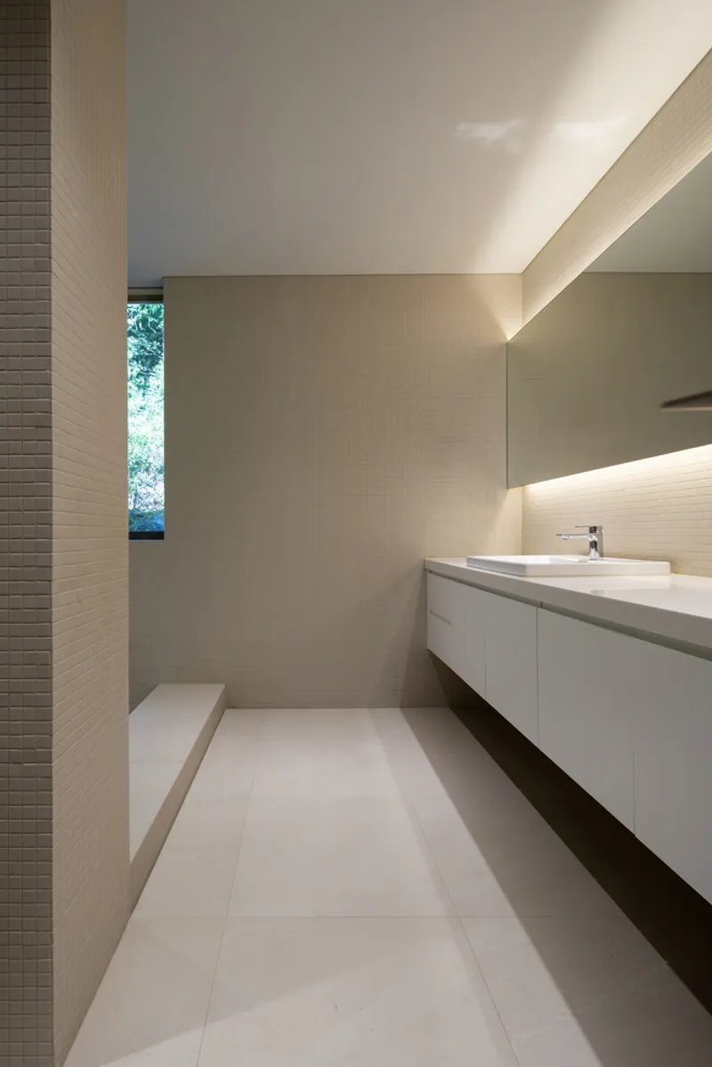 Bathroom vanity with backlit mirror, concealed lighting and narrow vertical window framing trees