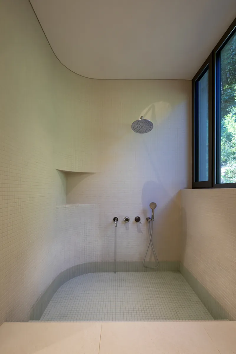 Sunken mosaic-tiled bathing pool with wall-mounted shower fixtures and curved ceiling plane