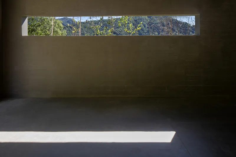 Interior room with horizontal window slot framing a distant hillside under afternoon light