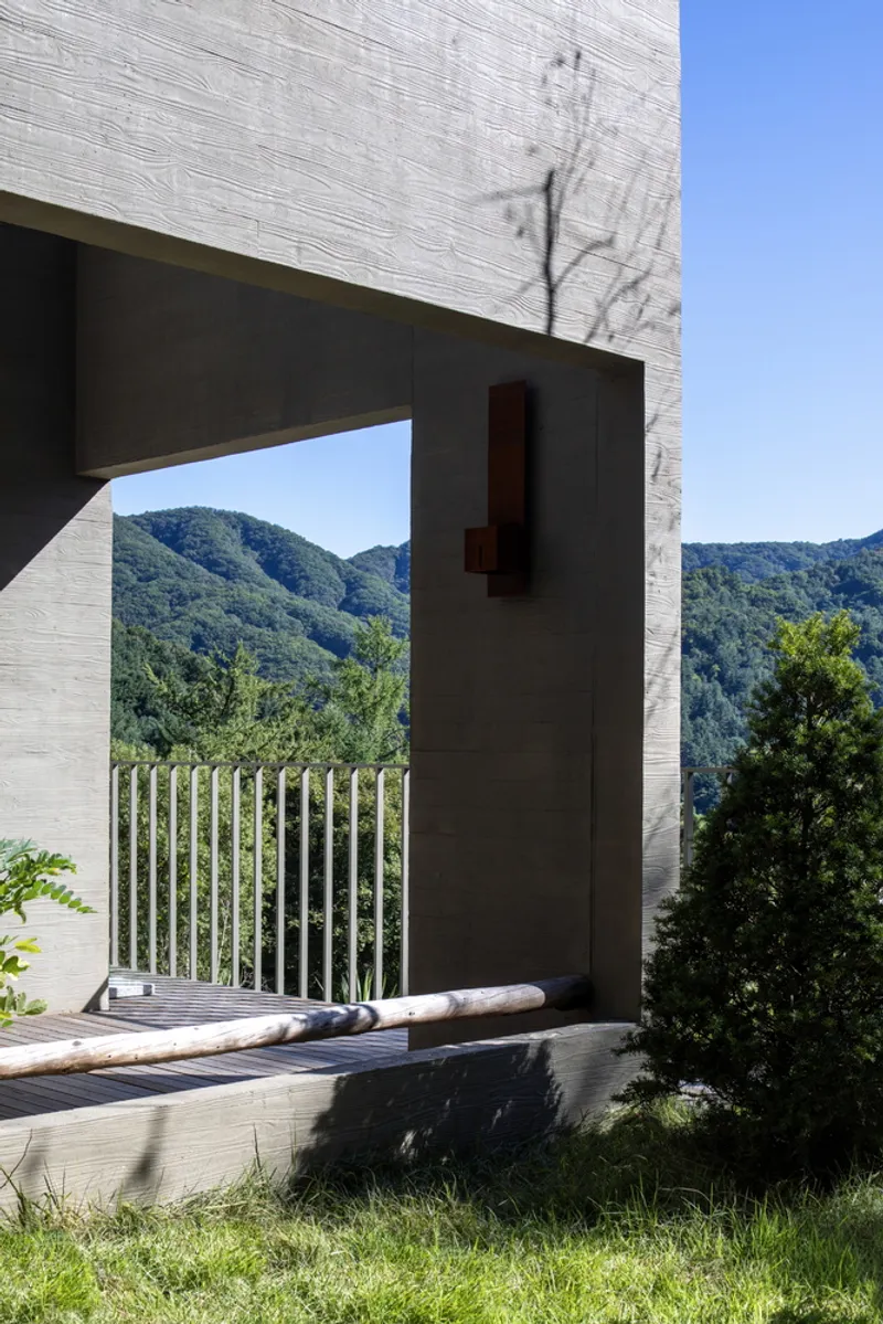 Cantilevered terrace with vertical metal railings framing a view of forested mountains under clear sky