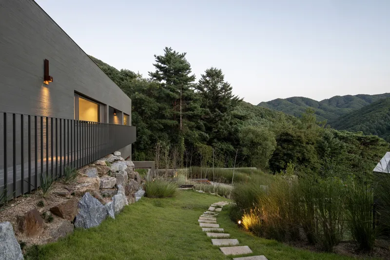Terraced lawn with stone stepping path and vertical slat screening below a curved concrete volume at dusk