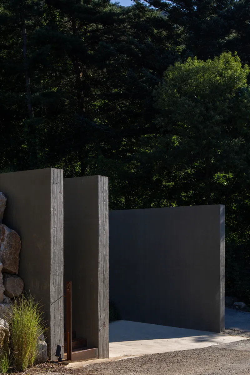 Entry courtyard with alternating dark metal and wood-textured concrete panels flanking a pivoting door