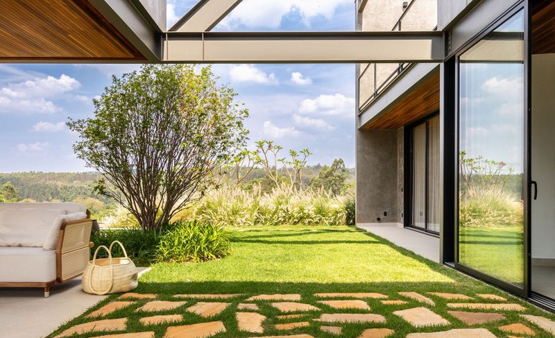 View from covered terrace through steel frame to stone-paved path crossing lawn with tree and distant hills