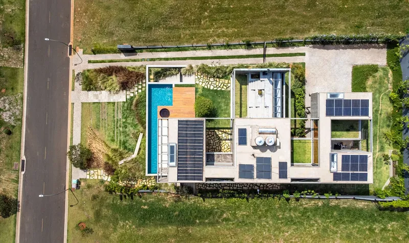 Aerial view of flat roof with solar panels, lap pool, and lawn patches beside residential street