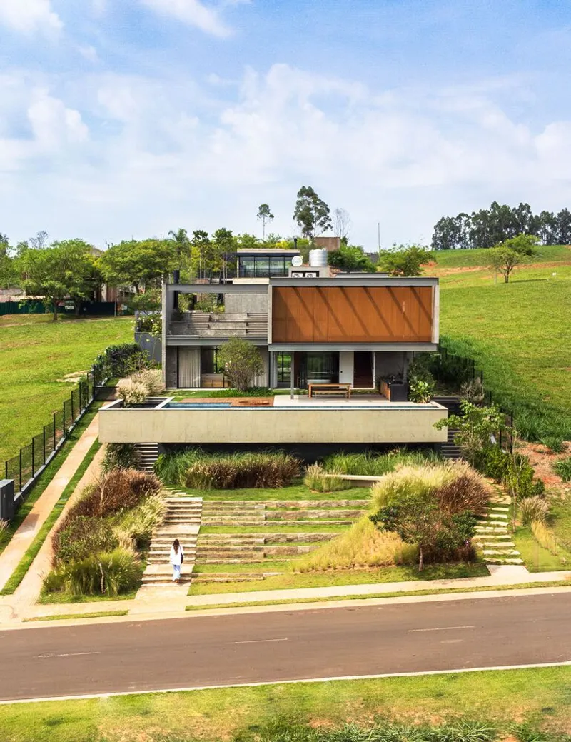 Street view of the terraced house with concrete and timber volumes set into a landscaped hillside