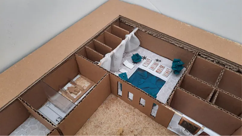 Top view of a cardboard model with white plaster courtyard and blue water feature under construction