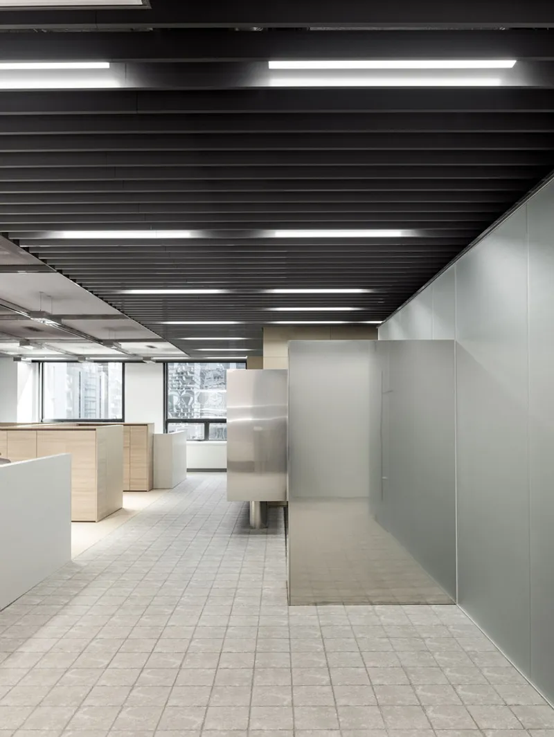 Glass-walled office pods with gray tile flooring under a linear black baffle ceiling