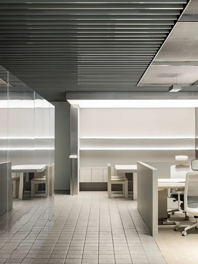 Low workstation dividers and office chairs under a black slatted ceiling with integrated lighting