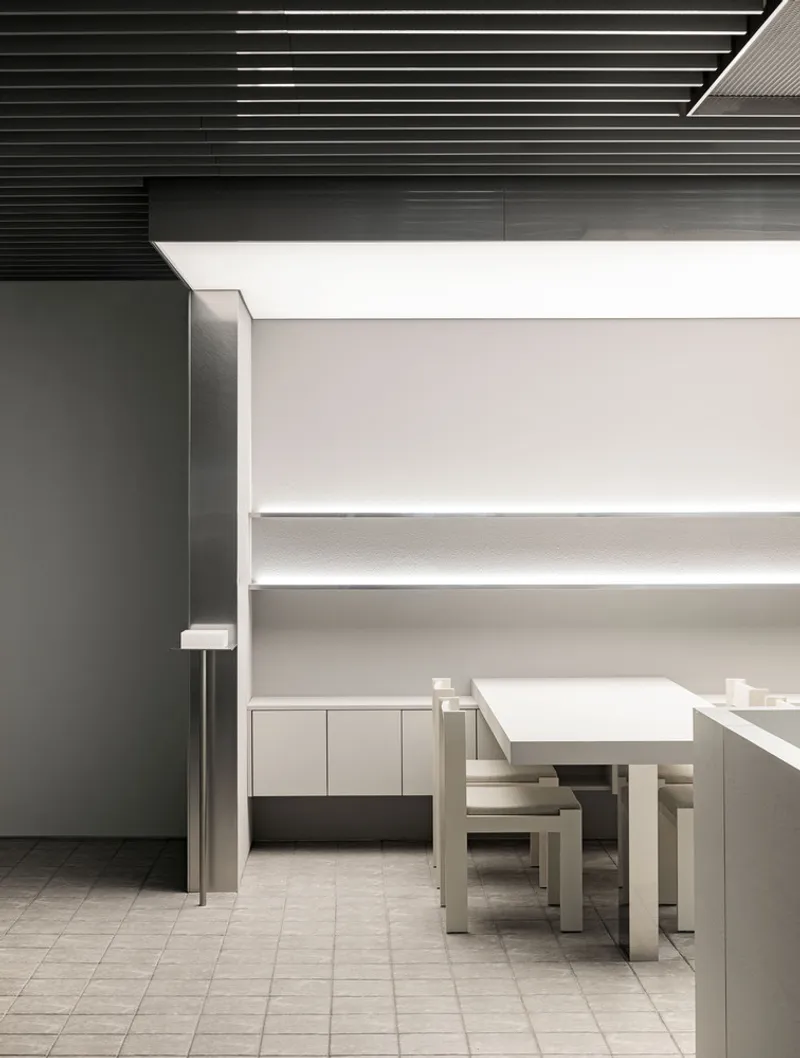 Breakout area with white benches and table beneath horizontal light strips and black ceiling baffles