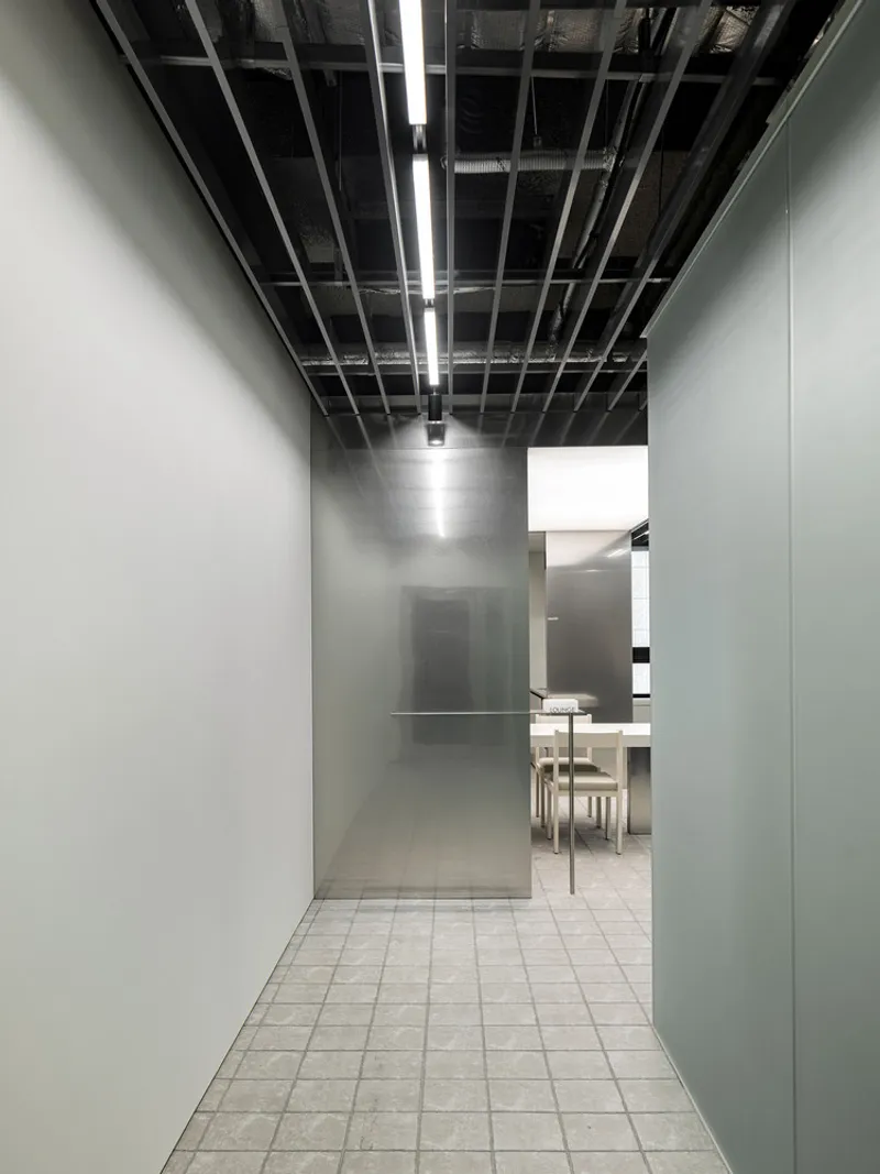 Narrow corridor with translucent glass partitions and exposed black ceiling structure with linear lighting