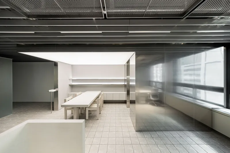 Open office space with pale timber tables beneath black louvered ceiling and frosted glass partitions