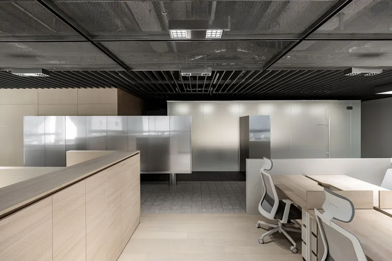 Workstations with light wood desks and translucent glass screens under exposed black baffle ceiling