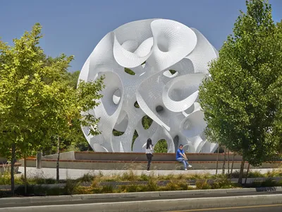 This architectural image showcases a large, white, geometric sculpture in a public space. The sculpt