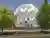 This architectural image showcases a large, white, geometric sculpture in a public space. The sculpt