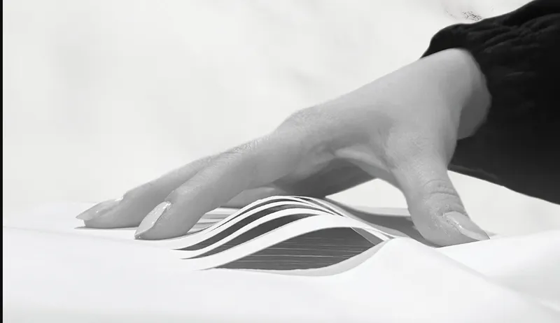 Hand touching a physical model showing the three curved roof volumes in layered sections