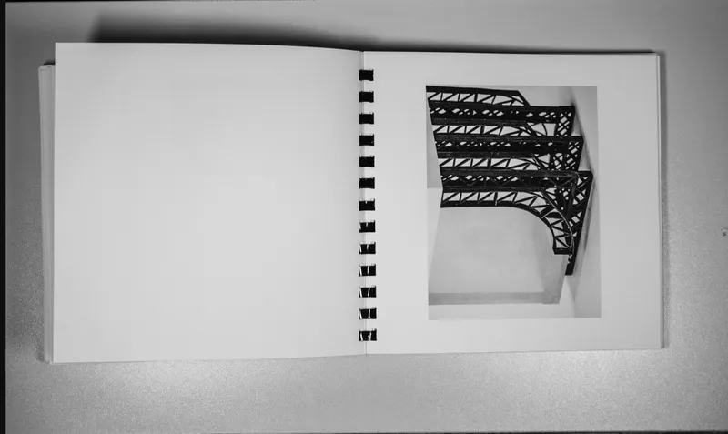 Photograph of an open spiral-bound sketchbook showing a truss structure model on white pages