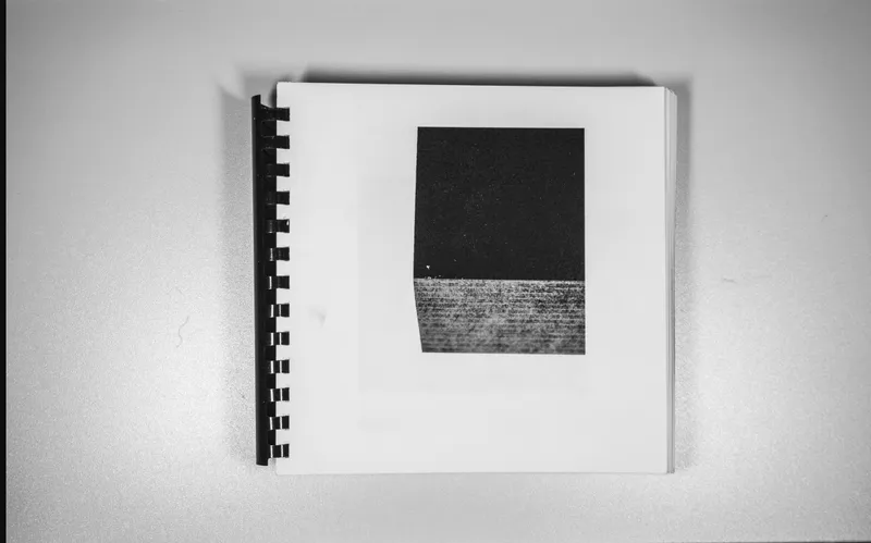 Photograph of an open spiral-bound sketchbook displaying a textured black square above a striated band