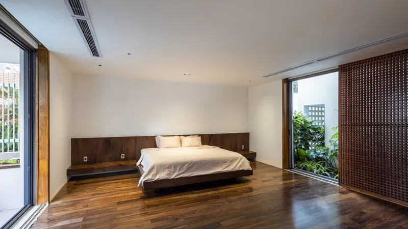 Bedroom with walnut platform bed and integrated headboard opening onto a planted terrace through sliding glass doors