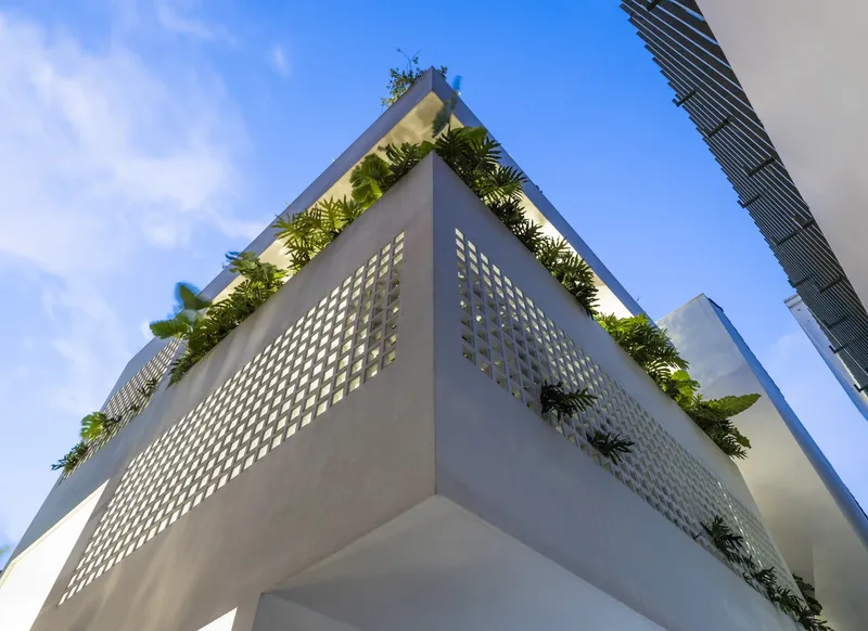 Corner facade with perforated concrete panels and rooftop planted terraces under a clear blue sky