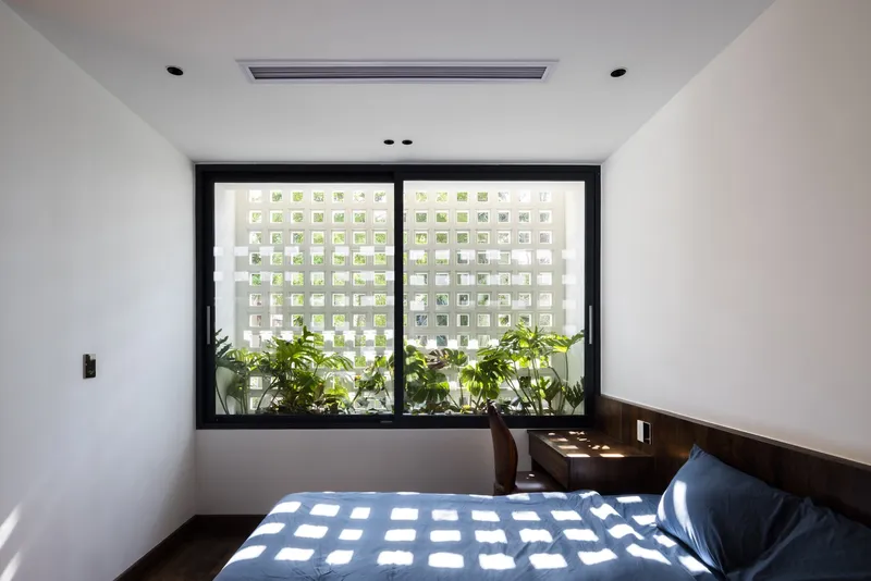 Bedroom window with perforated white screen filtering dappled sunlight onto potted plants on the sill