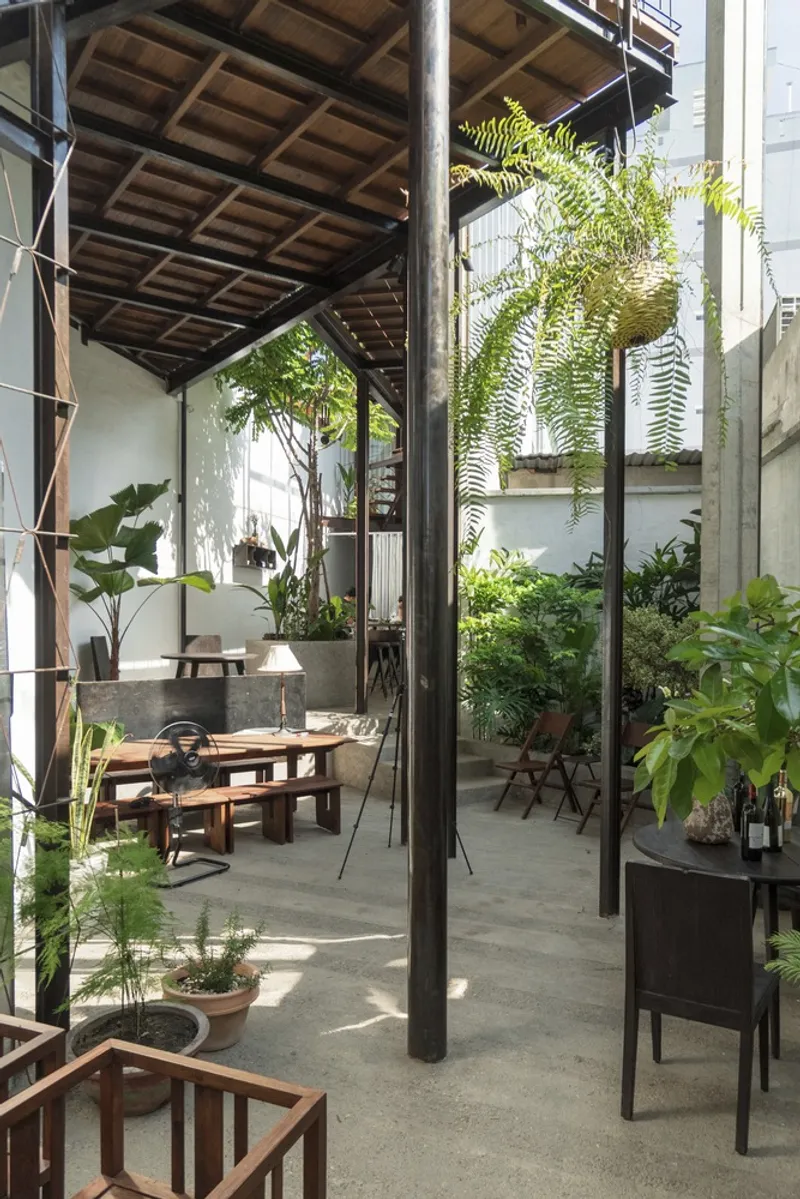 Courtyard with steel columns, timber ceiling, planted beds with ferns, and dappled sunlight on concrete floor