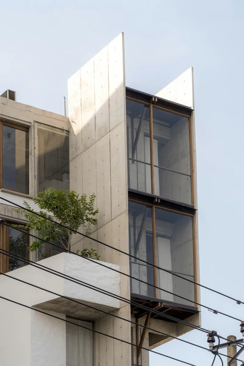 Concrete facade with vertical glazing panels framed in timber and angled parapet walls against an overcast sky