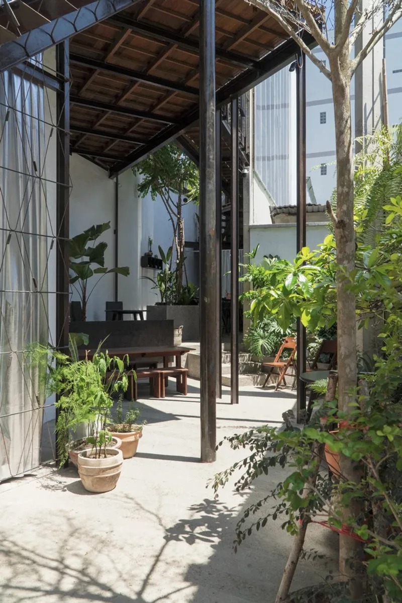 Covered patio with exposed timber ceiling and steel columns opening to a planted courtyard with potted greenery