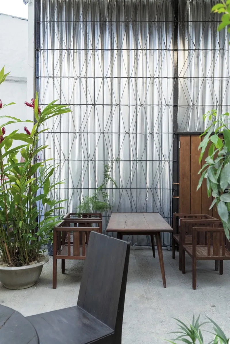 Wire trellis facade with bamboo planting and timber furniture on a concrete floor