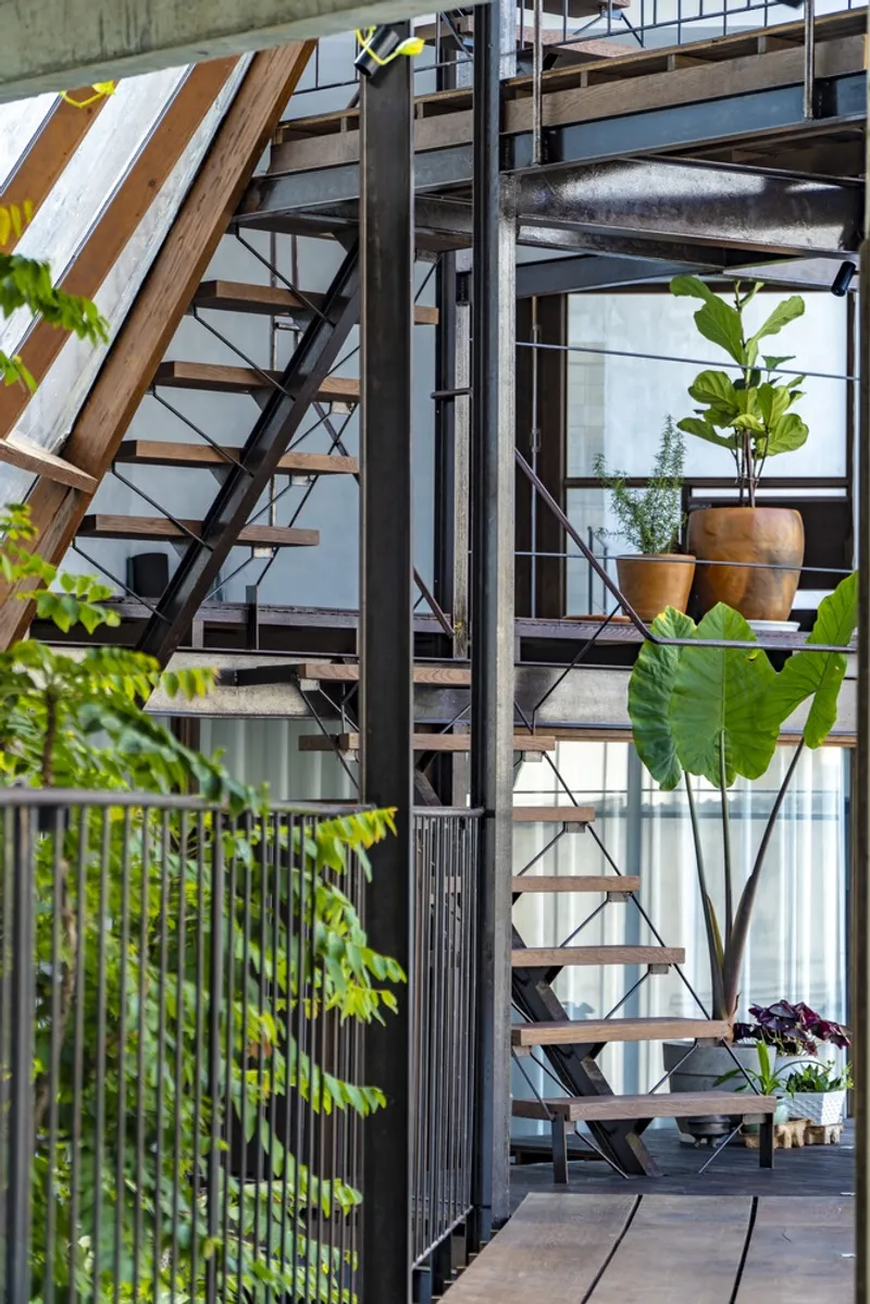 View through steel columns to an open timber staircase with potted plants on the landing