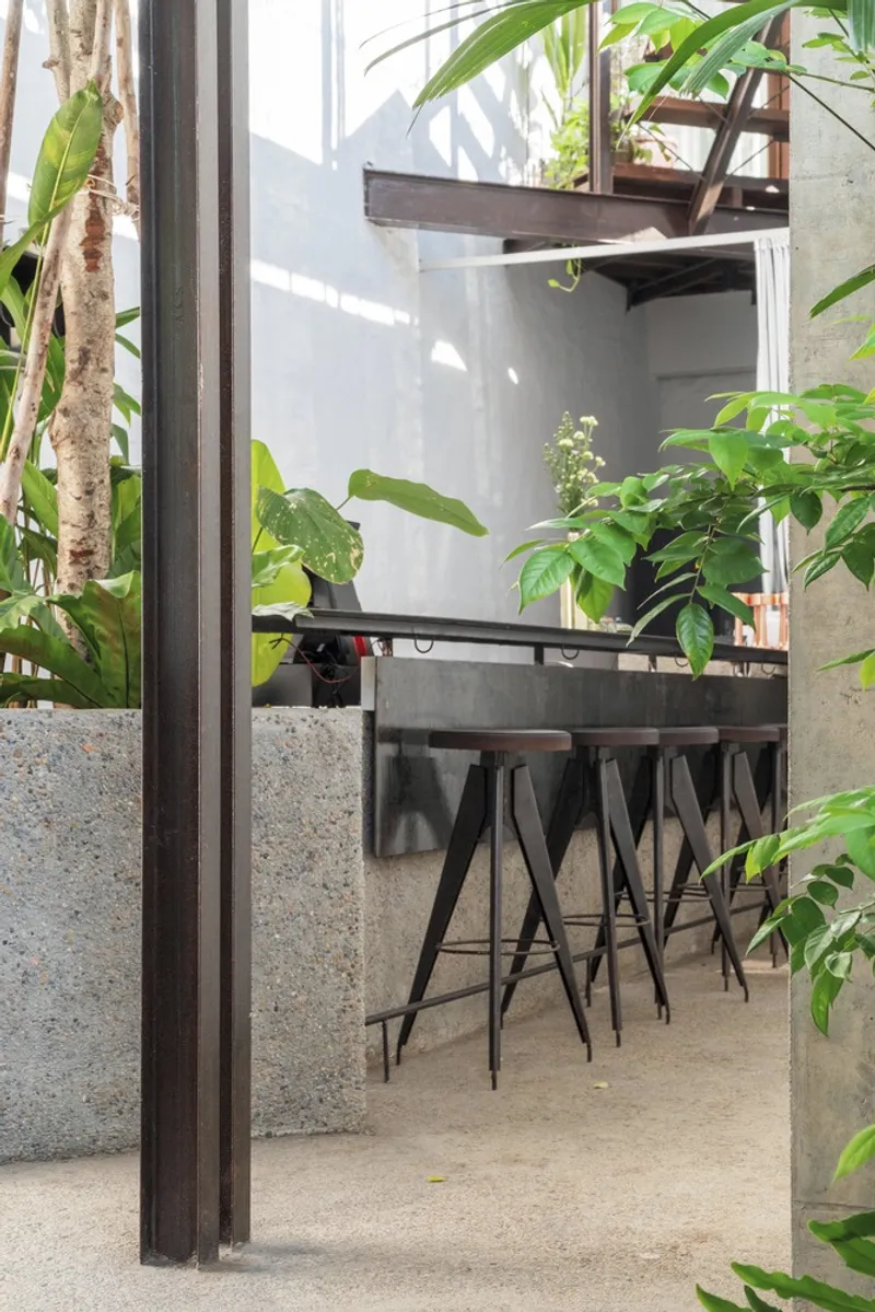 Concrete kitchen counter with metal bar stools framed by steel columns and tropical plants