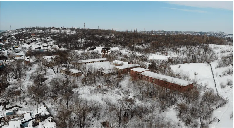 Aerial view of three linked brick pavilions nestled among bare trees in a snowy hillside landscape