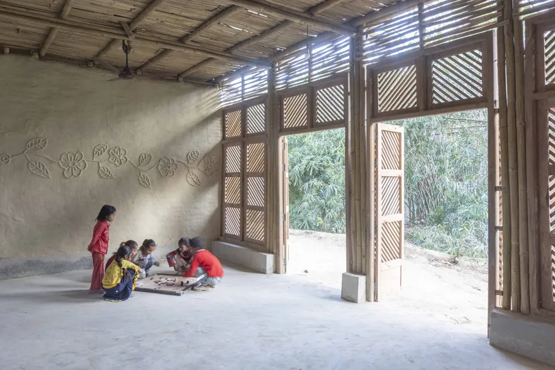 Interior space with slatted bamboo walls and ceiling casting light patterns on children playing below