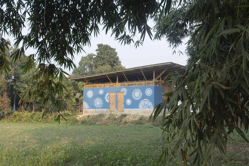 Facade with woven bamboo panels and white mandala patterns on blue walls framed by trees