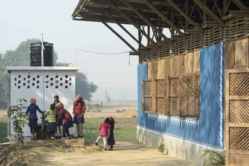 Exposed timber roof frame and bamboo screen walls with children gathering near a white latrine block