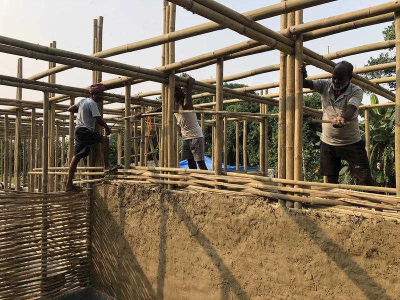 Construction workers assembling the bamboo frame structure and roof grid above earthen walls